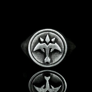 May include: A silver ring with a stylized bird design. The bird has a pointed head and wings that are spread out. The ring is set against a black background.