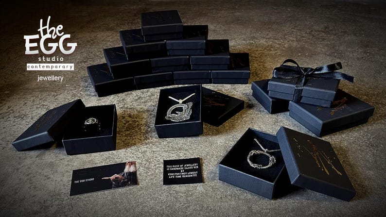 Może przedstawiać: Czarne pudełka z srebrną biżuterią w środku. Pudełka są ułożone na szarej powierzchni. Tekst "The Egg Studio Contemporary Jewellery" jest widoczny w lewym g&oacute;rnym rogu obrazu.