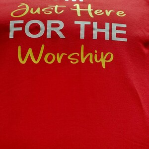 May include: Red t-shirt with the text "I'M Just Here FOR THE Worship" in white and gold lettering.