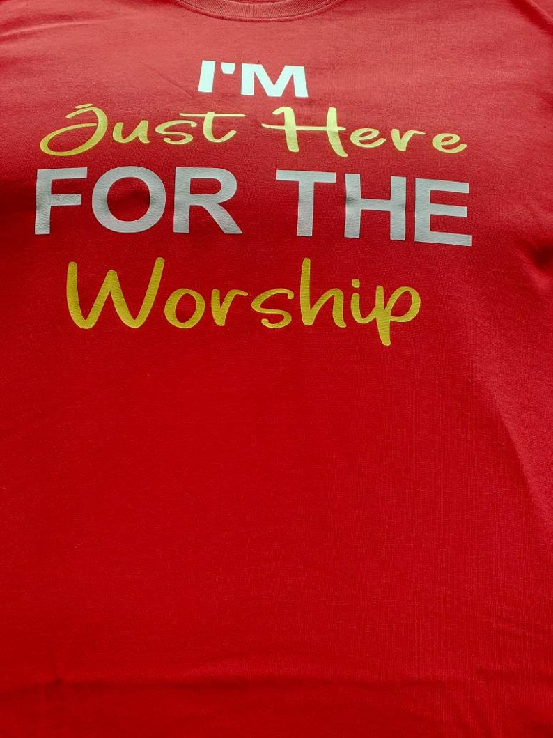 May include: Red t-shirt with the text "I'M Just Here FOR THE Worship" in white and gold lettering.