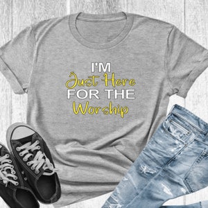 May include: A gray t-shirt with the text "I'm Just Here For The Worship" in yellow lettering.