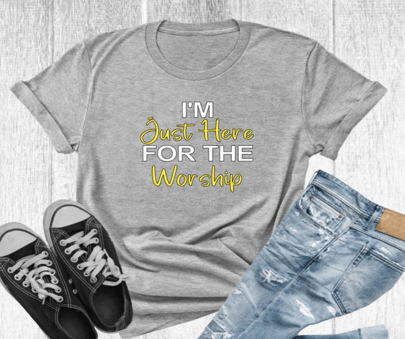 May include: A gray t-shirt with the text "I'm Just Here For The Worship" in yellow lettering.
