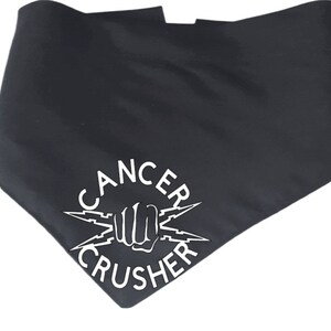 May include: Black pet bandana with the words "CANCER CRUSHER" in white, along with a fist and lightning bolt graphic. The bandana is a triangular shape, designed to be worn around a pet's neck.