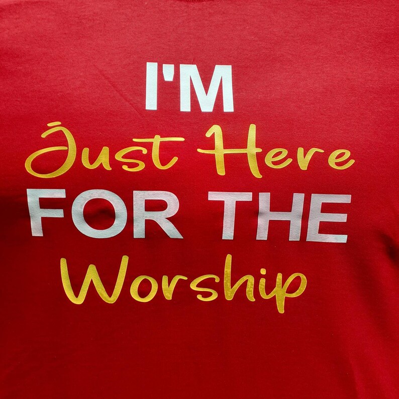 May include: Red t-shirt with the text "I'm Just Here For The Worship" in white and gold lettering.