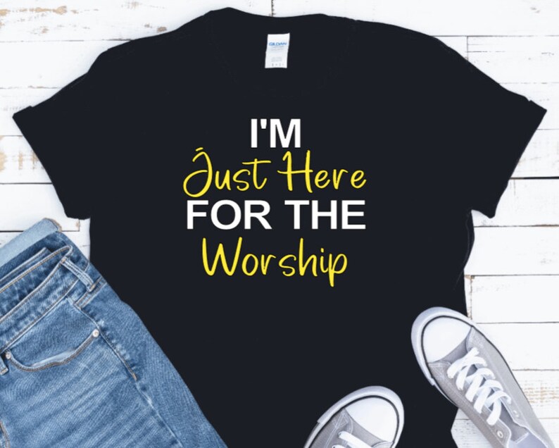 May include: Black t-shirt with white text that reads "I'm Just Here For The Worship" in yellow.