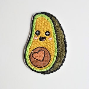 Peut inclure: Un patch brodé en forme d'avocat vert et marron avec un visage souriant et un cœur rose au centre.