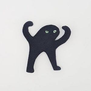 Könnte beinhalten: Ein schwarzer Katzenaufnäher mit grünen Augen, in einer von Memen inspirierten Pose, wird vor einem weißen Hintergrund gezeigt. Die Katze hat die Arme erhoben und ihr Körper befindet sich in einer trotzigen Haltung. Der Aufnäher ist wahrscheinlich aus Stoff und zum Aufnähen oder Aufbügeln auf Kleidung oder Accessoires bestimmt.