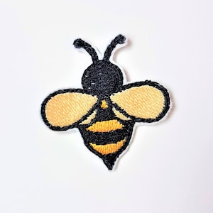 Puede incluir: Un parche bordado de abeja negro y amarillo sobre un fondo blanco.