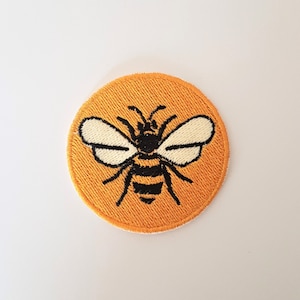 Peut inclure: Un patch brodé jaune avec un motif d'abeille noir et blanc.