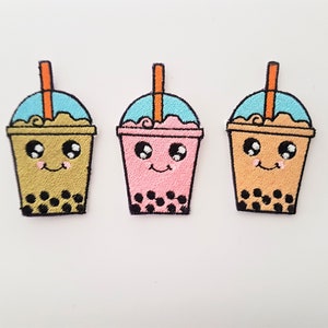 Könnte beinhalten: Drei gestickte Bügelbilder von niedlichen Bubble-Tea-Bechern mit lächelnden Gesichtern und Boba-Perlen. Die Becher sind in verschiedenen Farben: Gelb, Rosa und Orange.
