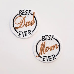 Peut inclure: Deux patchs ronds blancs brodés avec des contours noirs. Un patch dit "Best Dad Ever" en lettres dorées. L'autre patch dit "Best Mom Ever" en lettres dorées.
