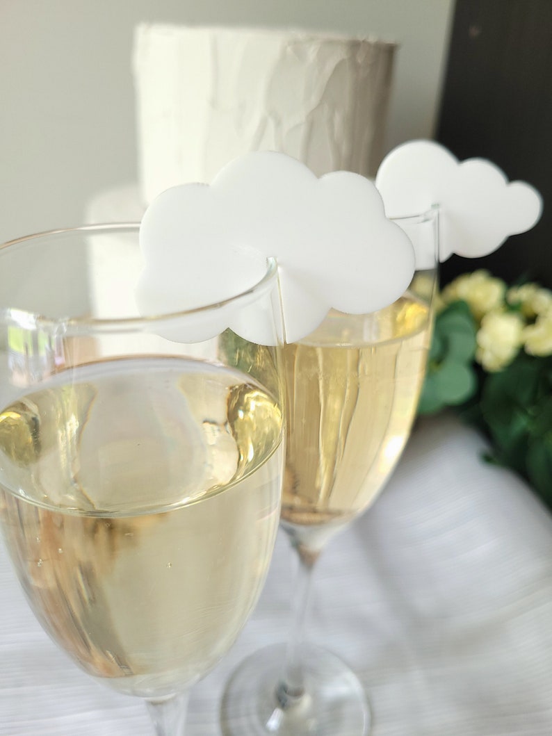 Peut inclure: Deux fl&ucirc;tes &agrave; champagne avec des marqueurs de boisson en forme de nuage blanc. Les fl&ucirc;tes sont remplies d'un liquide jaune p&acirc;le.