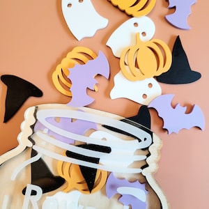 Könnte beinhalten: Ein hölzerner Halloween-Belohnungs-Glas mit einer durchsichtigen Vorderseite, verziert mit Fledermäusen, Geistern und Kürbissen. Das Glas trägt die Aufschrift "Reward Jar" auf der Vorderseite.