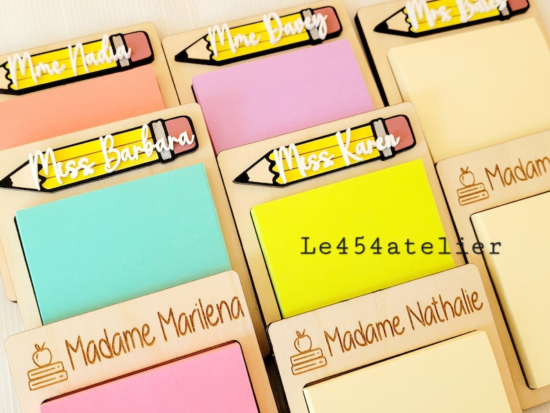 Peut inclure: Six blocs-notes en bois avec des noms personnalis&eacute;s et un design de crayon. Chaque bloc-notes a un bloc-notes adh&eacute;sif de couleur diff&eacute;rente. Les noms sur les blocs-notes sont "Mme Nadia", "Mme Dany", "Miss Barbara", "Miss Karen", "Madame Marilena" et "Madame Nathalie". Les blocs-notes sont fabriqu&eacute;s par Le454atelier.