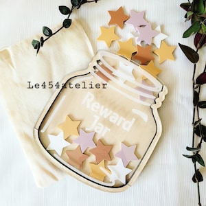 Pode incluir: Um pote de recompensa de madeira com uma frente de acrílico transparente, com o texto "Reward Jar". O pote está cheio de fichas em forma de estrela coloridas em tons de rosa, amarelo e marrom.