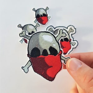 May include: Three embroidered iron-on patches featuring a skull with crossed bones wearing a red bandana. The patches are different sizes.
