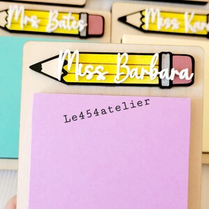 Peut inclure: Un bloc-notes en bois avec un motif de crayon jaune et le texte "Miss Barbara" et "Le454atelier". Le bloc-notes est muni d'un bloc-notes adh&eacute;sif rose.