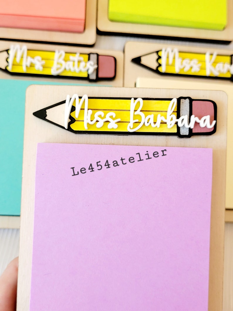 Peut inclure: Un bloc-notes en bois avec un motif de crayon jaune et le texte "Miss Barbara" et "Le454atelier". Le bloc-notes est muni d'un bloc-notes adh&eacute;sif rose.