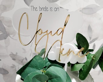 Peut inclure: Topper de gâteau en acrylique blanc avec inscription dorée "The bride is on cloud nine". Le topper est décoré de feuilles vertes.