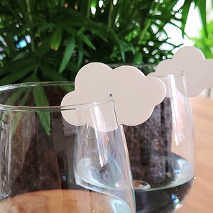 Peut inclure: Deux verres &agrave; vin en verre transparent avec des marqueurs de boisson en forme de nuage blanc. Les verres sont remplis d'un liquide bleu clair.