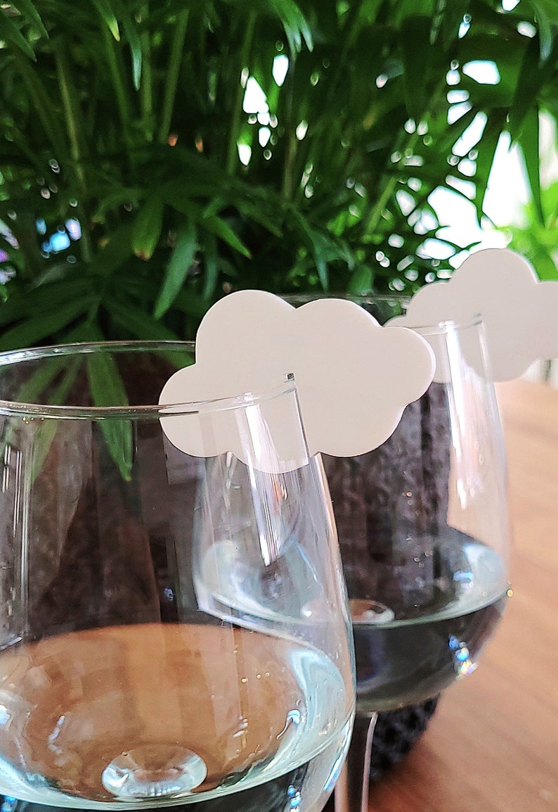 Peut inclure: Deux verres &agrave; vin en verre transparent avec des marqueurs de boisson en forme de nuage blanc. Les verres sont remplis d'un liquide bleu clair.