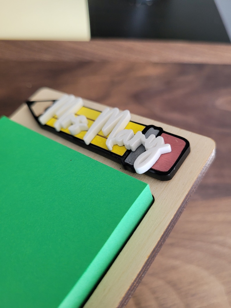 Peut inclure: Un porte-bloc-notes en bois avec un bloc-notes adh&eacute;sif vert. Le porte-bloc-notes pr&eacute;sente un design de crayon 3D avec les mots "Mrs. Mary" en lettres blanches.