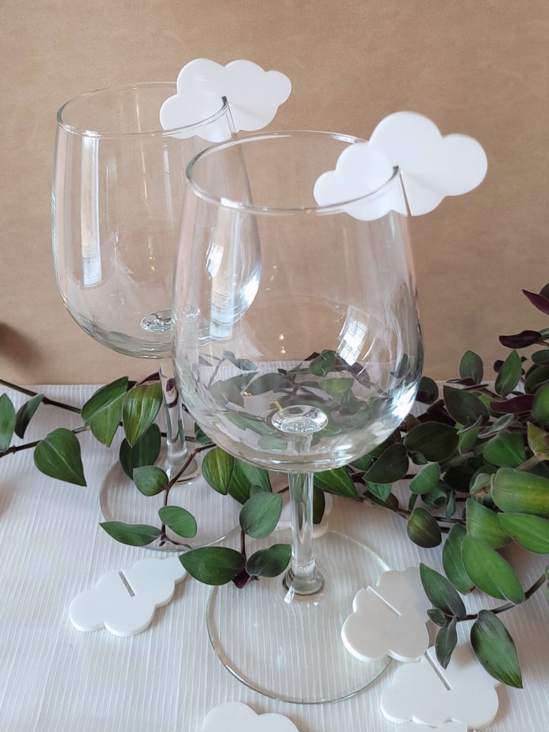 Peut inclure: Deux verres &agrave; vin transparents avec des marqueurs de boisson en forme de nuage blanc. Les marqueurs ont une petite fente au milieu pour maintenir la tige du verre.