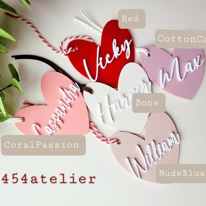 K&ouml;nnte beinhalten: F&uuml;nf herzf&ouml;rmige Acrylschilder mit verschiedenen Namen, die in Wei&szlig; darauf geschrieben sind. Die Schilder sind in verschiedenen Farben: Rot, Koralle, Rosa, Nude Blush und Knochen. Die Schilder sind mit den Farbnamen beschriftet: Rot, Korallenpassion, Zuckerwatte, Nude Blush und Knochen.