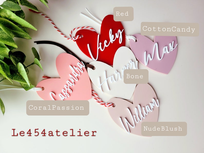 K&ouml;nnte beinhalten: F&uuml;nf herzf&ouml;rmige Acrylschilder mit verschiedenen Namen, die in Wei&szlig; darauf geschrieben sind. Die Schilder sind in verschiedenen Farben: Rot, Koralle, Rosa, Nude Blush und Knochen. Die Schilder sind mit den Farbnamen beschriftet: Rot, Korallenpassion, Zuckerwatte, Nude Blush und Knochen.
