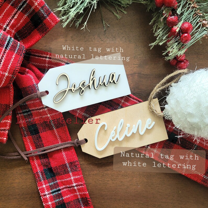 May include: Two wooden gift tags with names written on them. The top tag is white with the name "Joshua" written in brown lettering. The bottom tag is natural wood with the name "Celine" written in white lettering.