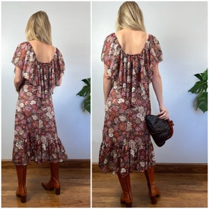 May include: A brown and pink floral print midi dress with a ruffled neckline and hem. The dress has short sleeves and a scoop back. The model is wearing brown boots.