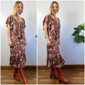 May include: A long floral print dress with a ruffled hem and short sleeves. The dress has a V-neckline and is made of a lightweight fabric. The model is wearing brown boots.