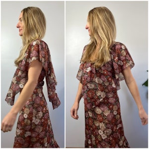 May include: A long, flowing floral print dress with a ruffled neckline and short sleeves. The dress has a brown, pink, and white floral pattern.