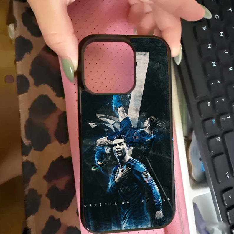 Puede incluir: Funda de tel&eacute;fono negra con un gr&aacute;fico de Cristiano Ronaldo con uniforme de f&uacute;tbol azul. La funda tiene un borde negro y el nombre del jugador est&aacute; impreso en la parte inferior. El fondo es un dise&ntilde;o oscuro y abstracto.