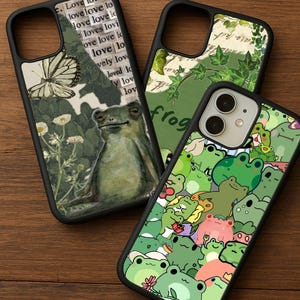 May include: Three black phone cases with unique designs. One case features a frog illustration with text, another has a butterfly and floral design, and the third showcases a pattern of various green frogs.