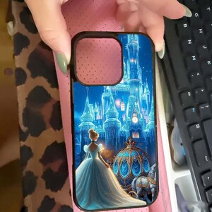 May include: Black phone case featuring a fairytale scene with a princess in a blue gown, a horse-drawn carriage, and a castle. The case has a black border and a cutout for the camera.