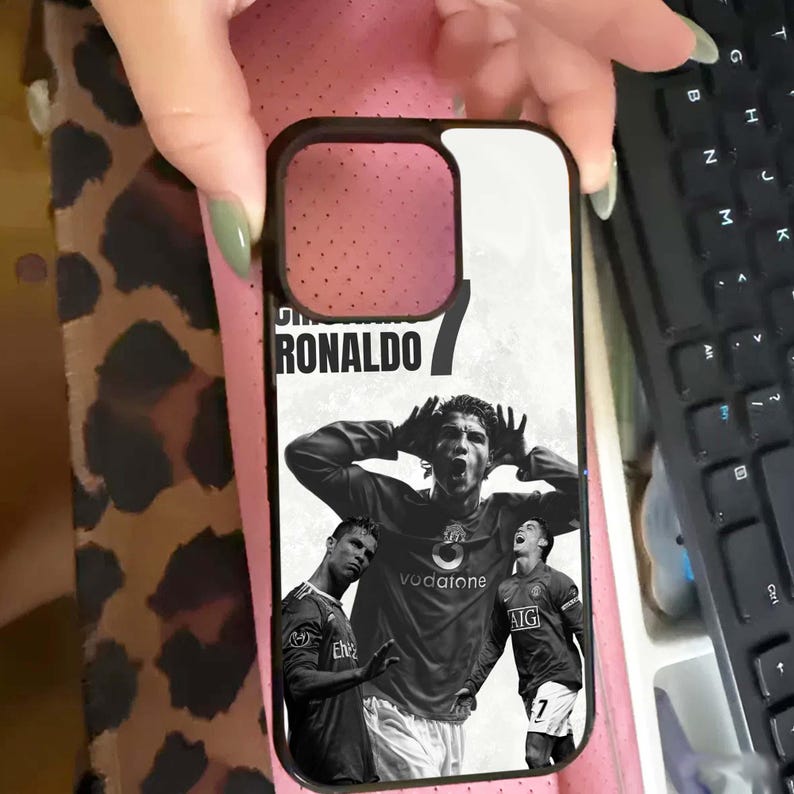 Puede incluir: Funda de tel&eacute;fono negra con im&aacute;genes en blanco y negro de Cristiano Ronaldo con la camiseta del Manchester United. El nombre "RONALDO" est&aacute; impreso en la parte superior. Tambi&eacute;n es visible el n&uacute;mero "7".