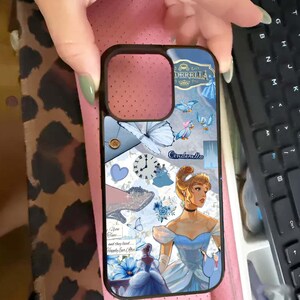 May include: A black phone case featuring a Cinderella design. The case has a blue and white color scheme with illustrations of Cinderella, birds, a clock, and the text "Cinderella". The case also includes the text "Upon a time...and they lived...Happily Ever After".