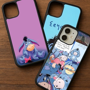 May include: Three black phone cases with Eeyore designs. One case shows Eeyore sitting, another has the word "Eeyore" in blue, and the third displays multiple Eeyore images with quotes like "Nobody ever does."