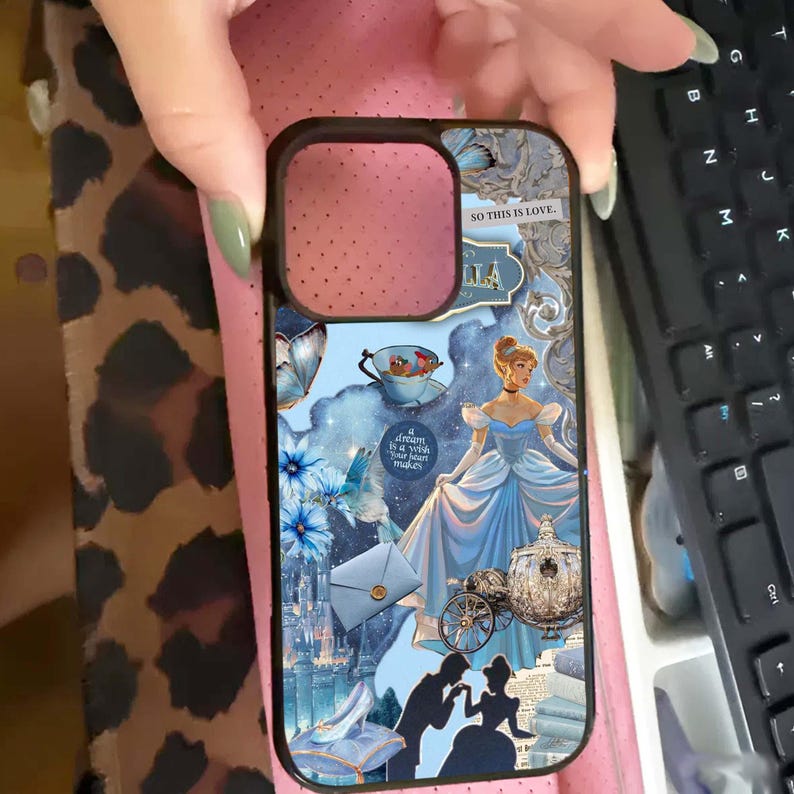 May include: A black phone case featuring a collage of Cinderella-themed imagery. The design includes Cinderella in a blue gown, a carriage, and the text "SO THIS IS LOVE." Additional elements include a teacup, flowers, and a castle.