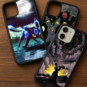 Könnte beinhalten: Drei schwarze Handyhüllen mit farbenfrohen Designs. Eine Hülle zeigt eine blau-schwarze Kreatur vor einem mondbeschienenen Ozean. Eine andere zeigt eine schwarze Kreatur mit gelben Akzenten und grünen Sternen. Die dritte Hülle zeigt eine schwarze Kreatur vor einem feurigen, bewölkten Hintergrund.