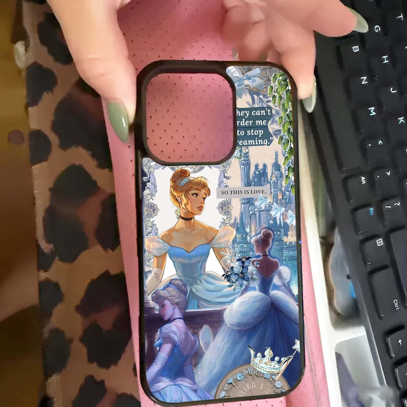 May include: Black phone case featuring a Cinderella-themed design. The case displays Cinderella in a blue gown, with text that reads "hey can't order me to stop dreaming" and "SO THIS IS LOVE."