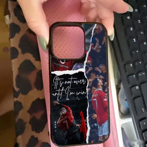 Puede incluir: Funda de tel&eacute;fono negra con un collage de un jugador de f&uacute;tbol con una camiseta roja. La funda tiene el texto "It's not over until I'm win!" y el nombre y el n&uacute;mero del jugador. La funda la sostiene una persona.