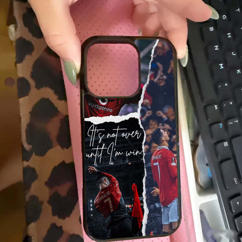 Puede incluir: Funda de tel&eacute;fono negra con un collage de un jugador de f&uacute;tbol con una camiseta roja. La funda tiene el texto "It's not over until I'm win!" y el nombre y el n&uacute;mero del jugador. La funda la sostiene una persona.