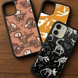 May include: Three phone cases with black borders and dinosaur skeleton designs. One case has a brown background with dinosaur skeletons, another has an orange background with dinosaur bones, and the third has a black background with dinosaur skeletons and leaves. The Studio Maleo logo is visible.