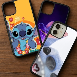 May include: Three black phone cases with colorful designs. One case features a cartoon character with a floral lei against a yellow background. Another has a purple floral design, and the third has a close-up of a blue character.