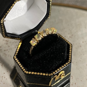 May include: A gold ring with five opal stones set in a row. The ring is in a black ring box.