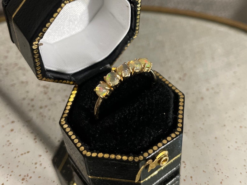 May include: A gold ring with five opal stones set in a row. The ring is in a black ring box.