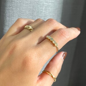 May include: A gold ring with a row of small, white gemstones. The ring is on a person's finger.