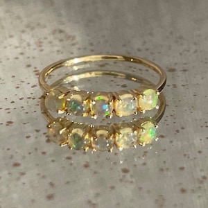 May include: A gold band ring with five round opal gemstones set in a row. The opals are iridescent and have a milky white color.